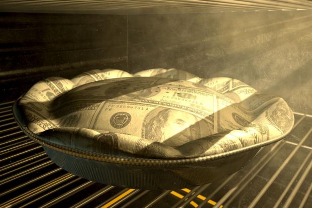 A pie baking in a dark oven with sideways lighting appears to be made out of U.S. bills.